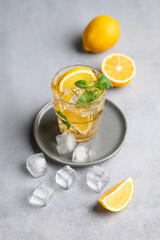 Iced tea with lemon, mint and ice in a glass on a light background with citrus fruits.
