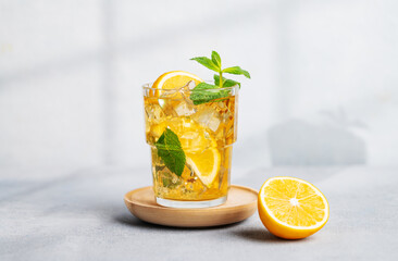 Fototapeta premium Iced tea with lemon, mint in a glass on light background with shadow and citrus fruits.