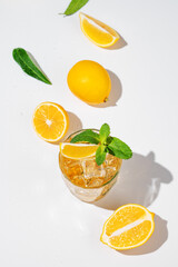 Flat lay of Iced tea with lemon and mint on white background with a shadow and citrus fruits.