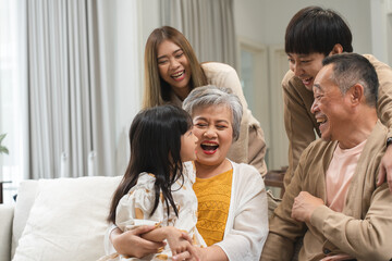 Asian cute little girl sitting on sofa with grandparent and young parent, talking, smiling...