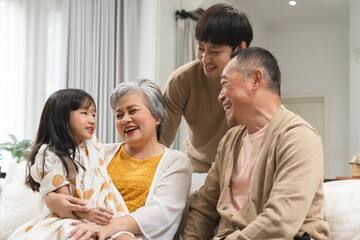 Asian cute little girl sitting on sofa with grandparent and young father, talking, smiling...