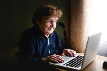 An elderly woman is working on a laptop.