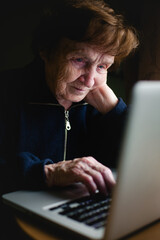 An old woman sits with her laptop. - 779665496
