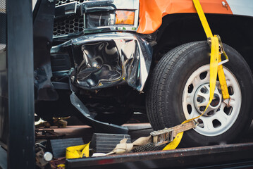 Damaged bumper front fender on pickup truck by car accident carrier on flatbed rollback slide tilt tray of tow truck with yellow ratchet strap tie down, collision, insurance claim concept, Texas