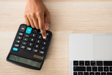 Top closeup view of hand using calculator beside laptop. Home finance concept.