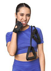Athletic young Caucasian woman with resistance band on studio background biting fingernails,...