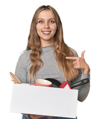Blonde Caucasian woman moving with a box on studio backdrop person pointing by hand to a shirt copy...