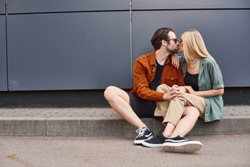 A romantic scene of a sexy couple sitting on the ground, sharing a passionate kiss.