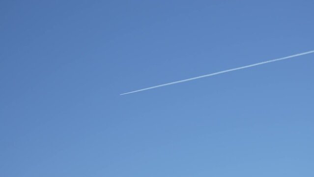 Distant jet plane flying on high altitude on clear blue sky with white trace of contrail