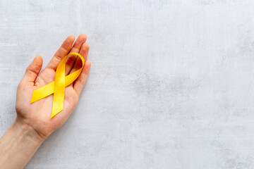 Yellow ribbon symbol of bone cancer with hands. Medical support and prevention - 779682836