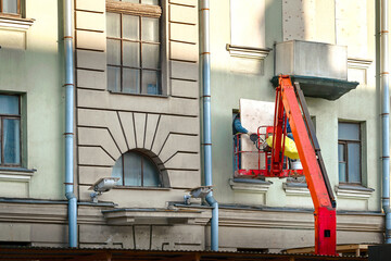 Workers in crane bucket board up window before reconstruction work. Plywood guards for windows, protect windows on construction site. Construction workers attaching plywood for window protection.