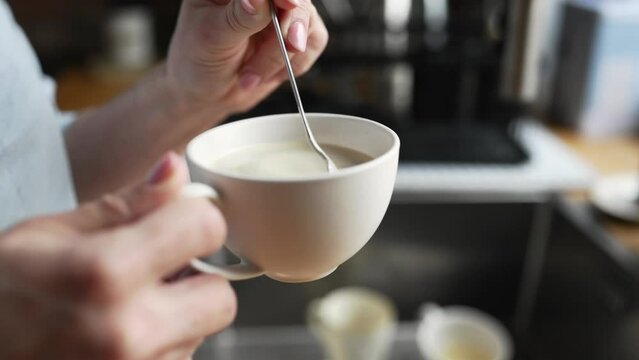 Girl hand stiring coffee cappuccino in cup at kitchen for breakfast. Morning espressoo latte beverage at home