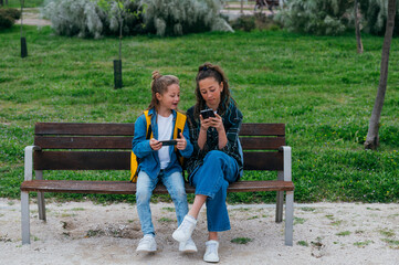 Little boy accompanied by his older sister using smart phone sitting on a bench.