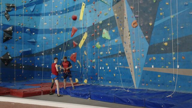 Wide shot of instructor explaining how to use rope to man with prothetic leg during personal training session in climbing gym