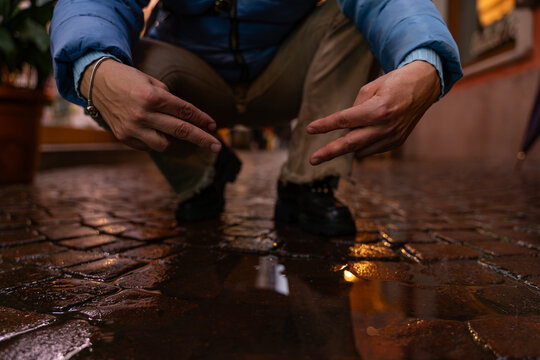 man in blue sneakers bending over a puddle showing the victory sign with his hands on a city street
