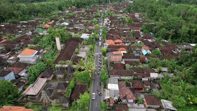 Aerial view of village street, motorbikes and trucks full of people in white ride behind procession. Celebration of Melis day at Bali, unusual traffic on the road at big religious event