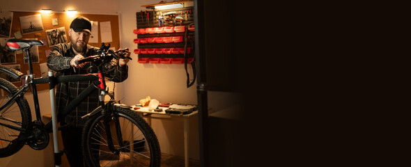 Handsome man in cap, handyman standing with a bicycle in the garage at home. Bicycle repairing and diy concept