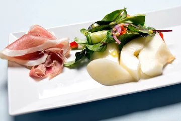 Foto op Plexiglas Voorgerecht van meloen met rauwe ham en salade op een wit bord © ArieStormFotografie