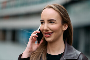 Business Woman With Phone Near Office. Portrait Of Beautiful Smiling Female In Fashion Office Clothes Talking On Phone While Standing Outdoors. Phone Communication. 