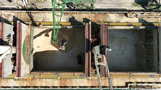 Unloading dry cargo ship by cranes in port. Aerial view cargo hold