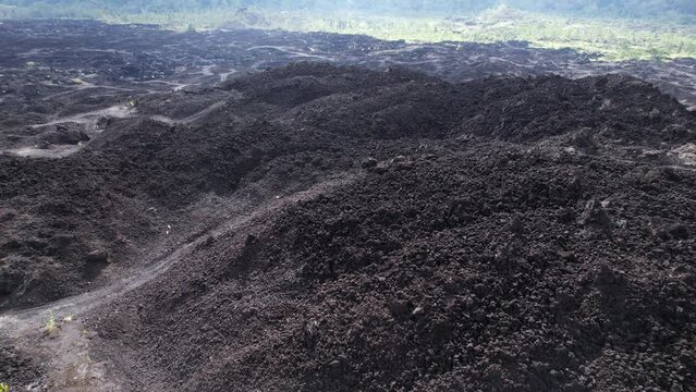 Old lava field at bottom of Batur volcano, black field with vehicle traces somewhere. Open mining remains visible at the area, unusual places and landscapes of Bali island from the air, drone shot