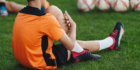 Young Boys in Sports Uniform Sitting and Stretching on Grass Field. Kids in Soccer Club on Training Unit. Kids Play Team Sports. Boy Pulling Knee To Chest During Soccer Fitness Session
