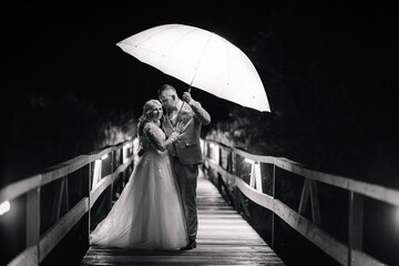 Valmiera, Latvia - August 13, 2023 - A bride and groom stand under an umbrella on a bridge at...
