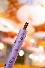 Fototapeta premium Close-up of a packet of Chinese or japanese chopsticks for eating oriental Asian food with a warm, multicolored blurred background of an Asian restaurant.