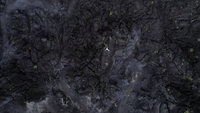 Small figure of man lying spread out on black lava, camera quickly flies up over huge hardened field at foot of Mount Batur volcano. Scenic landscapes remains deserted and impressive