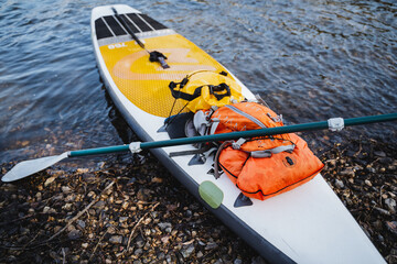 A close-up of a SUP board is moored to a sandy shore, things are collected in a dry bag, a paddle...