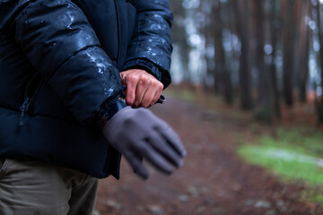 Unrecognizable hands donning snow and mountain gloves, amidst blurred forest backdrop, eco-tourism