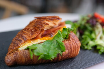 4K Breakfast Scene. A woman is eating a croissant with bacon and scrambled eggs at breakfast.