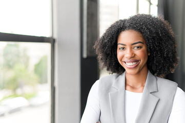 A radiant African-American businesswoman smiles warmly in an office setting, showcasing a blend of...