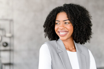 A radiant African-American businesswoman smiles confidently, standing in a modern office...