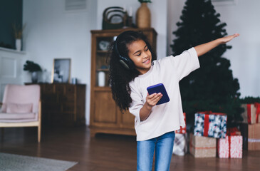 Smiling black girl playing with smartphone while dancing in living room
