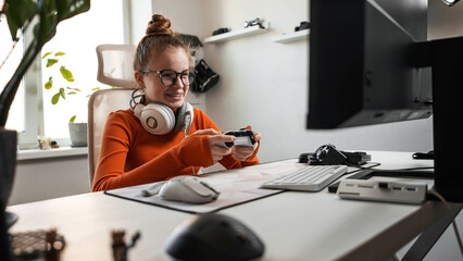 Teenage girl is sitting in a comfortable computer chair, holding a white gamepad in her hands and...