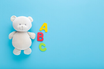 Smiling cute soft white teddy bear and colorful abc letters on light blue table background. Pastel color. Time to learning. Closeup. Empty place for text. Top down view.