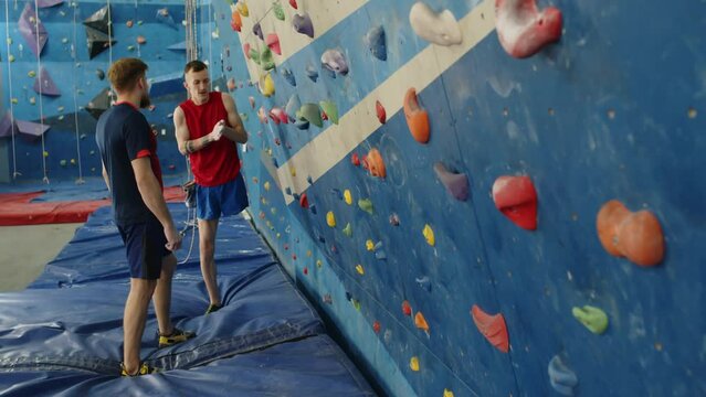 Man with disability talking with friend, then climbing wall together while practicing bouldering in indoor gym