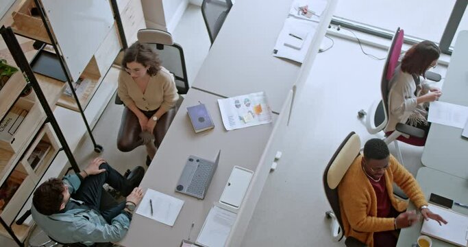 An overhead view captures multiethnic, cross-generational colleagues engaged in various business activities in a bright, contemporary office setting, highlighting the dynamism of the modern workplace.