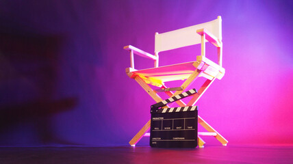 Director chair and clapper board in purple pink light.