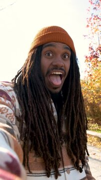 African American young man with dreadlocks smiling and taking selfies in a sunny day of autumn.