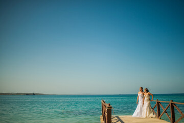 mujeres usando su vestido de bodas y caminando por un muelle a la orilla del mar 