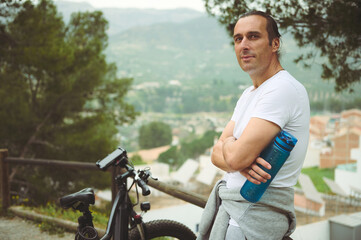 Handsome athletic man in white t-shirt, holding a bottle with water, smiling confidently looking at...
