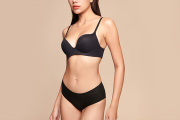 Fototapeta premium Confident beautiful young asian woman posing in black lingerie on beige background, Perfect body,