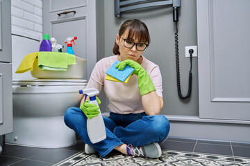 Tired woman sitting on the floor after cleaning the bathroom