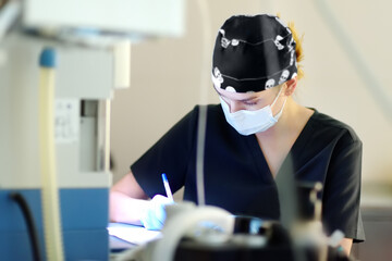Intern surgeon records the progress of the operating room in a journal. Wearing an operating gown the anesthesiologist describes the operation in a chart.