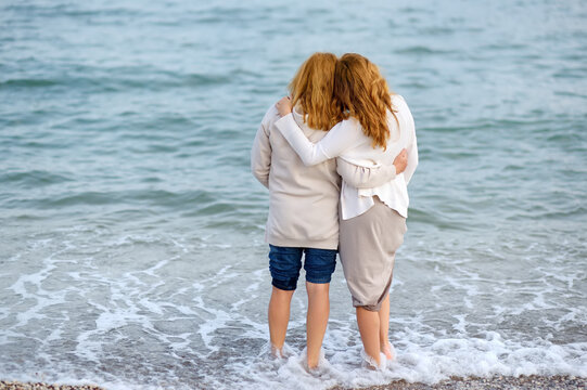 Redhead senior mother and her beautiful adult daughter are walking together. A happy meeting of a mom and her grown child. Cute woman tenderly hugs her mature mother on Mother's Day