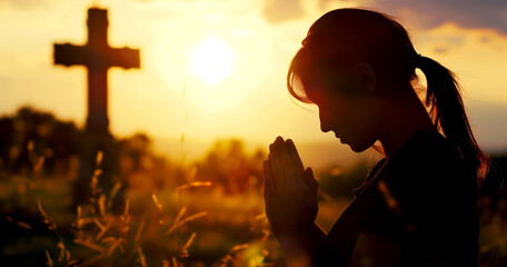 A woman is praying at the cross in the evening sunlight. - obrazy, fototapety, plakaty
