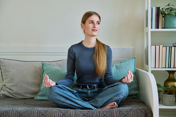 Young teenage relaxed female sitting in lotus position, meditating at home