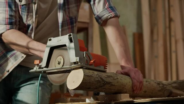 Male woodworker working in garage. Man professional carpenter working with wooden materials in workshop sawing wood using electric circular saw.